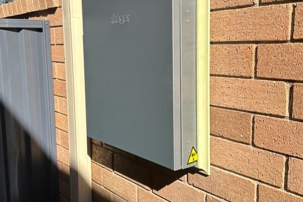 Grey electrical switchboard mounted on an exterior brick wall – Marmont Electrical