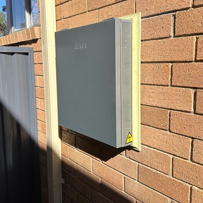 Grey electrical switchboard mounted on an exterior brick wall – Marmont Electrical